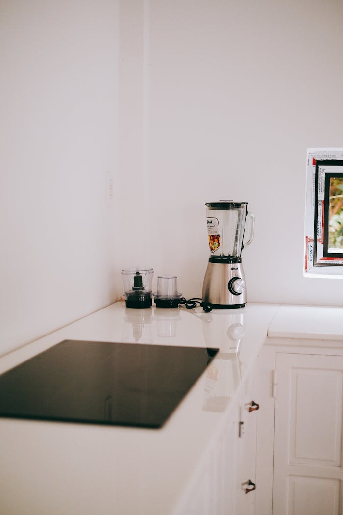 about-me-img Stylish kitchen corner featuring a sleek blender and induction stove on a white countertop.