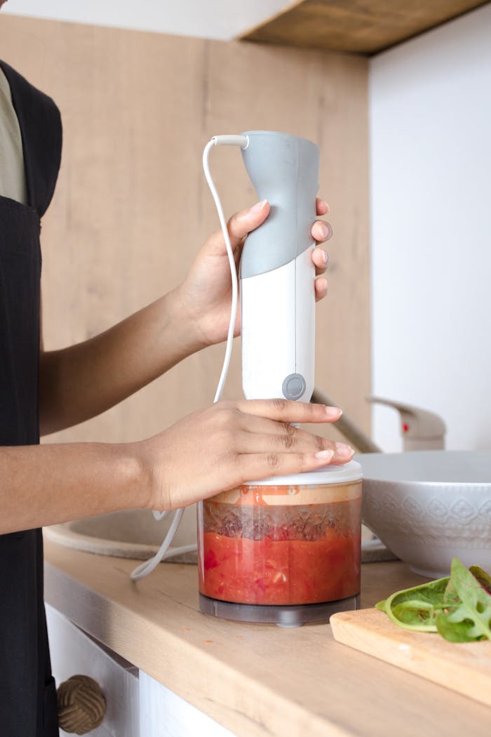 contact-img A person blending vegetables with a hand blender in a modern kitchen setting.